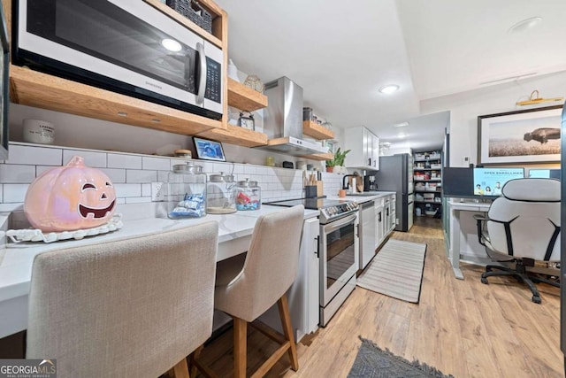 kitchen featuring light hardwood / wood-style flooring, decorative backsplash, white cabinets, appliances with stainless steel finishes, and exhaust hood