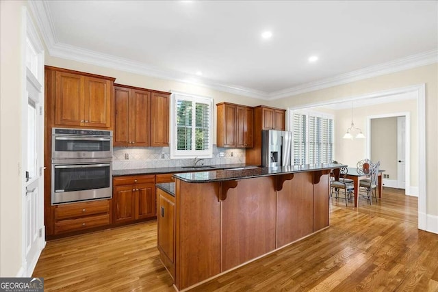 kitchen with ornamental molding, a center island, appliances with stainless steel finishes, a breakfast bar, and hardwood / wood-style floors