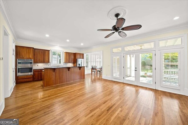 kitchen featuring ceiling fan, light hardwood / wood-style flooring, ornamental molding, appliances with stainless steel finishes, and a center island