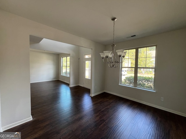 spare room featuring dark wood-type flooring and an inviting chandelier