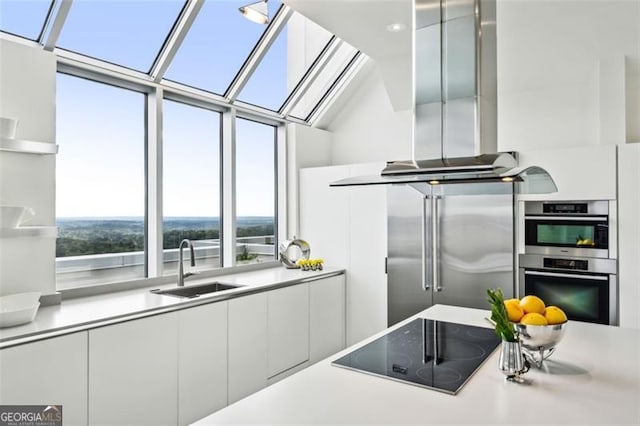 kitchen with white cabinets, sink, a skylight, island range hood, and appliances with stainless steel finishes