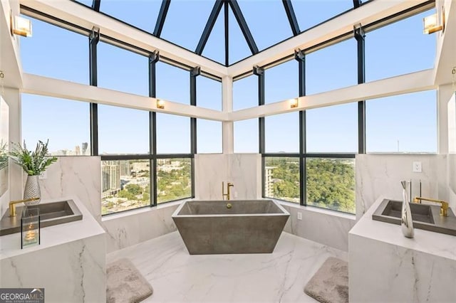 bathroom featuring a towering ceiling, a tub to relax in, plenty of natural light, and sink