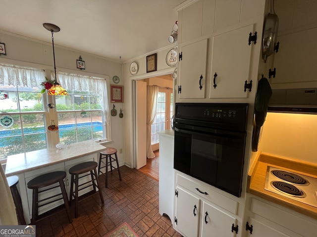 kitchen featuring a healthy amount of sunlight, black oven, hanging light fixtures, and white cabinetry