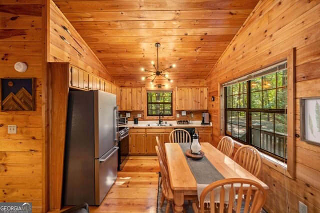 kitchen featuring stainless steel appliances, lofted ceiling, light hardwood / wood-style flooring, and wooden walls