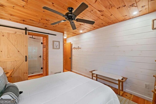 bedroom featuring wooden walls, ceiling fan, wood ceiling, wood-type flooring, and a barn door