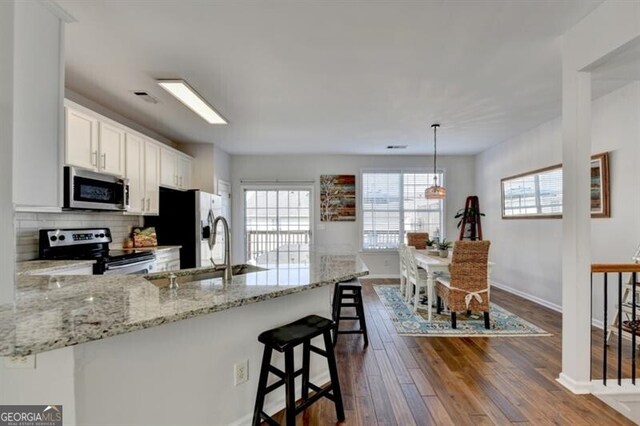 kitchen featuring dark hardwood / wood-style flooring, a breakfast bar area, white cabinetry, appliances with stainless steel finishes, and decorative light fixtures