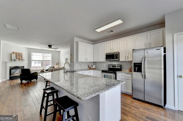 kitchen with appliances with stainless steel finishes, kitchen peninsula, light hardwood / wood-style floors, and white cabinets