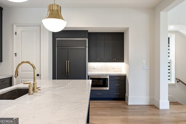 kitchen with sink, light hardwood / wood-style flooring, built in appliances, light stone countertops, and decorative backsplash