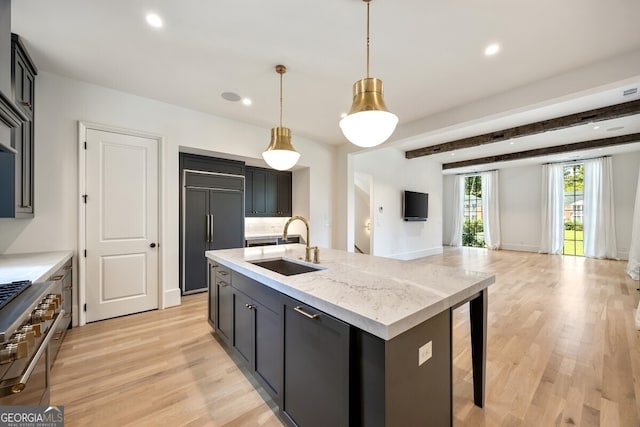 kitchen featuring premium appliances, a kitchen island with sink, light hardwood / wood-style flooring, sink, and hanging light fixtures