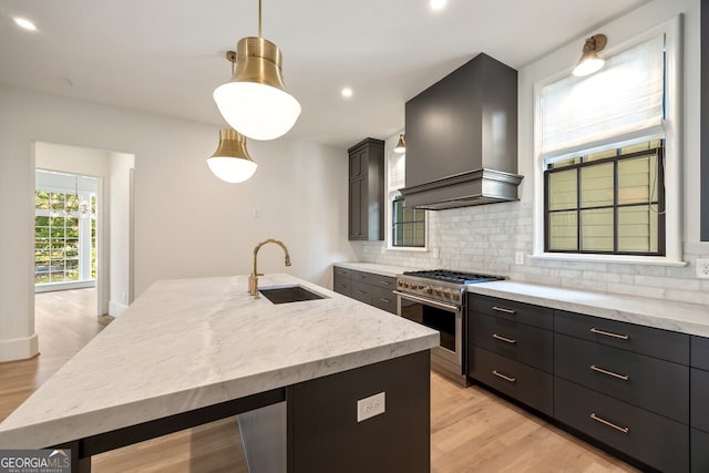 kitchen featuring custom exhaust hood, hanging light fixtures, sink, high end stainless steel range, and a kitchen island with sink