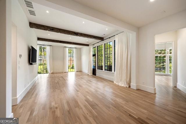 unfurnished living room featuring beam ceiling, a wealth of natural light, and light hardwood / wood-style flooring