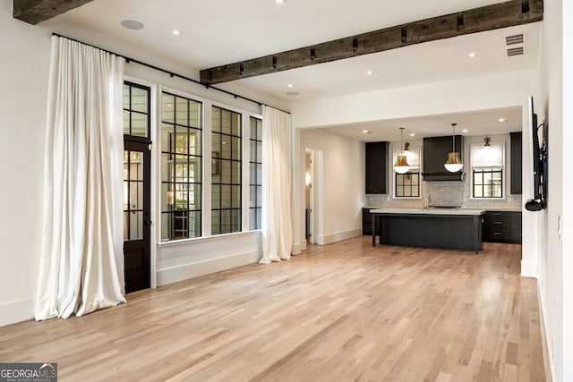 unfurnished living room with light hardwood / wood-style floors, beamed ceiling, and a wealth of natural light