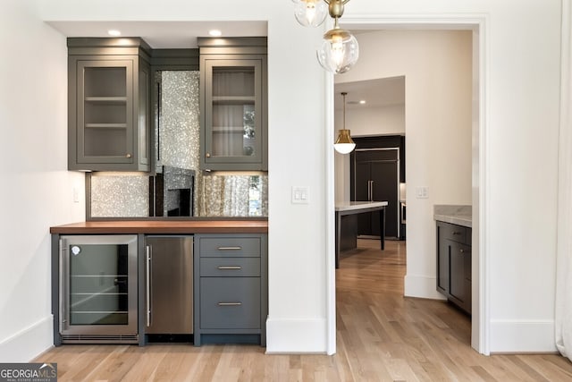 bar featuring gray cabinetry, tasteful backsplash, beverage cooler, light hardwood / wood-style flooring, and wood counters