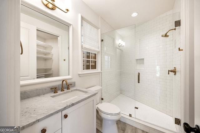 bathroom featuring a shower with door, vanity, and toilet