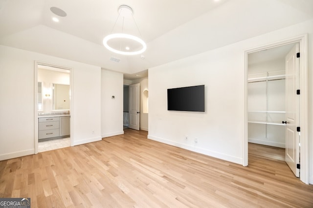 unfurnished bedroom featuring a closet, connected bathroom, light hardwood / wood-style floors, and lofted ceiling