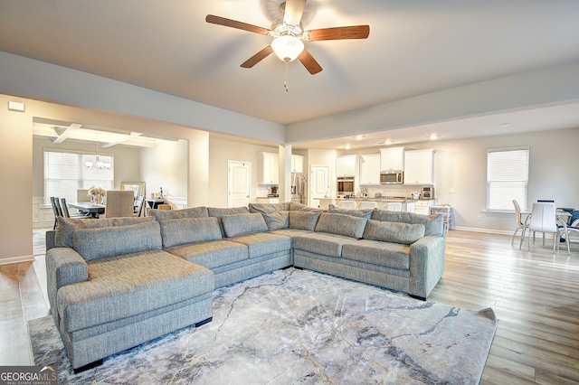 living room featuring ceiling fan with notable chandelier and light hardwood / wood-style floors