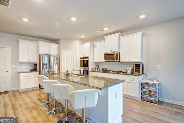 kitchen with a center island with sink, light wood-type flooring, stainless steel appliances, and white cabinets