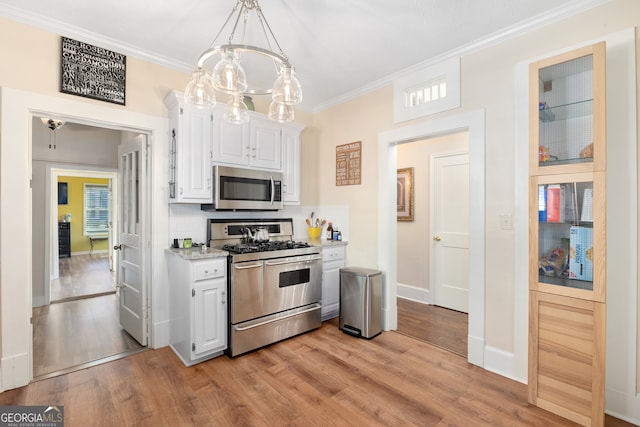 kitchen with stainless steel appliances, white cabinets, light hardwood / wood-style floors, pendant lighting, and ornamental molding