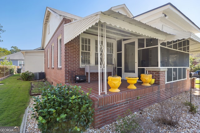 rear view of house with a sunroom, a patio, central AC unit, and a lawn