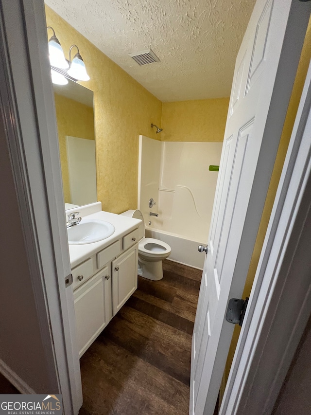 full bathroom featuring hardwood / wood-style floors, vanity, shower / bathing tub combination, toilet, and a textured ceiling