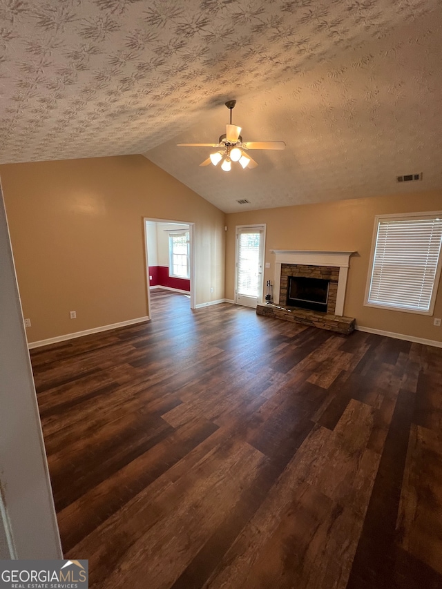 unfurnished living room with ceiling fan, dark hardwood / wood-style flooring, vaulted ceiling, a fireplace, and a textured ceiling