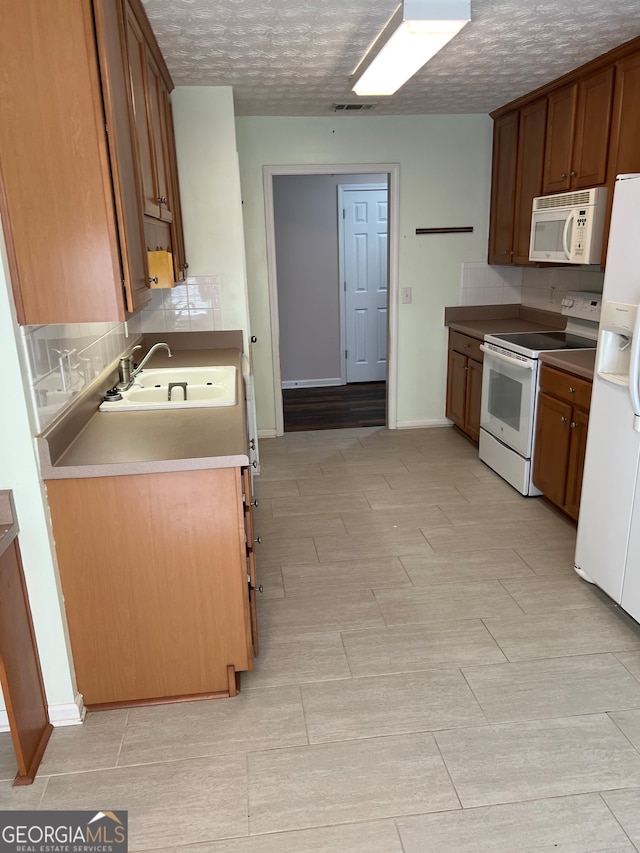 kitchen with decorative backsplash, white appliances, sink, and a textured ceiling