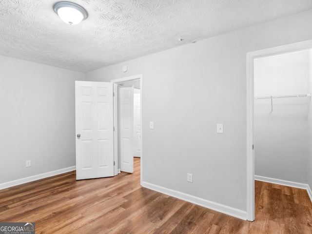 unfurnished bedroom featuring hardwood / wood-style floors, a walk in closet, a textured ceiling, and a closet