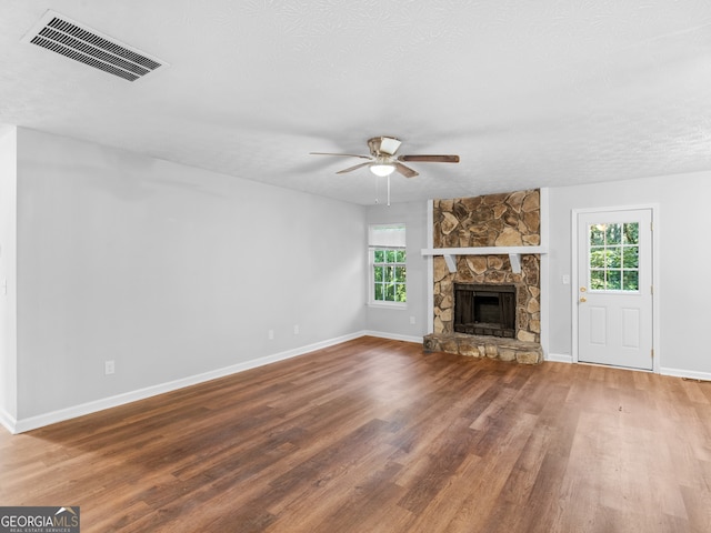 unfurnished living room featuring a stone fireplace, a healthy amount of sunlight, wood-type flooring, and ceiling fan