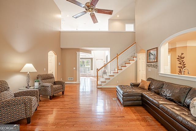 living room with crown molding, ceiling fan, a towering ceiling, and light hardwood / wood-style flooring