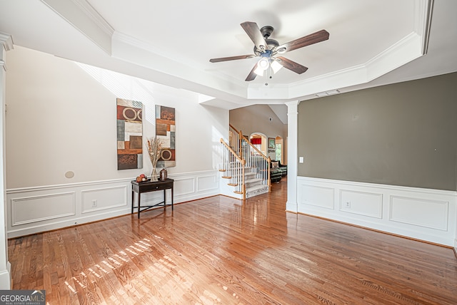 interior space with ceiling fan, crown molding, a raised ceiling, decorative columns, and hardwood / wood-style flooring