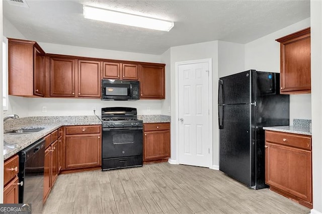 kitchen with light hardwood / wood-style flooring, light stone counters, sink, black appliances, and a textured ceiling