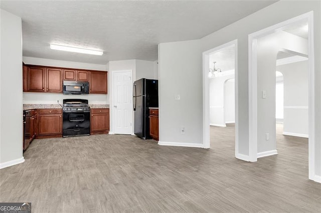 kitchen with light hardwood / wood-style floors, black appliances, and a notable chandelier