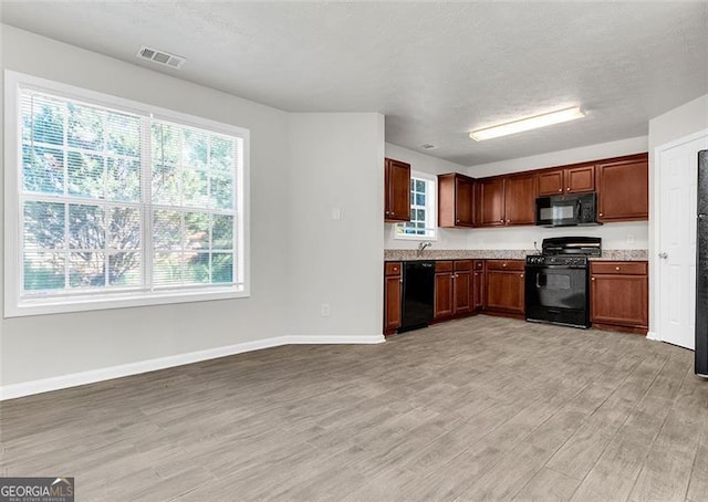 kitchen with a textured ceiling, black appliances, and light hardwood / wood-style flooring