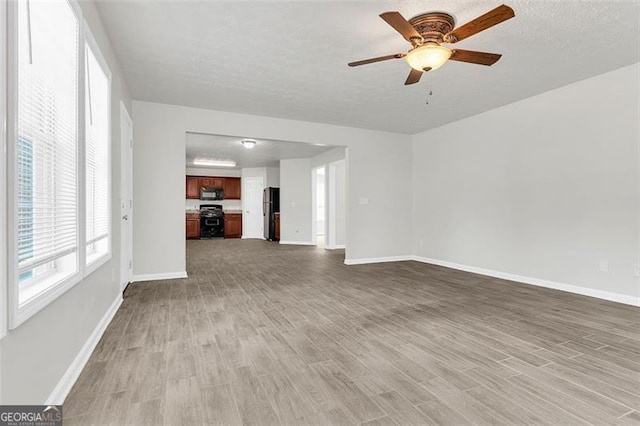 unfurnished living room with ceiling fan, a textured ceiling, and light wood-type flooring