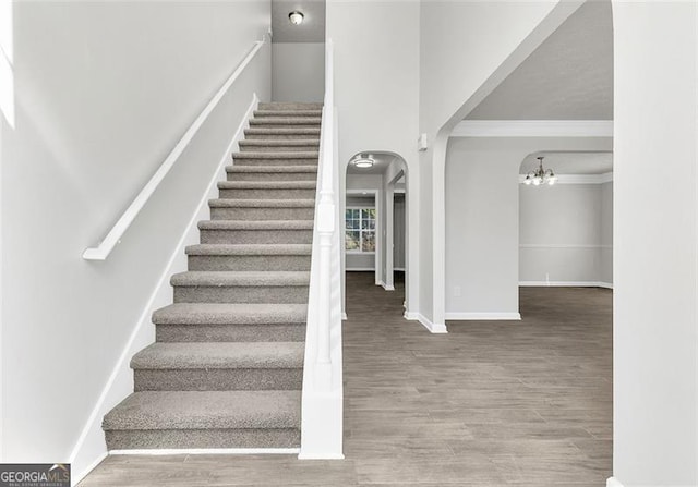 staircase featuring ornamental molding, an inviting chandelier, and wood-type flooring