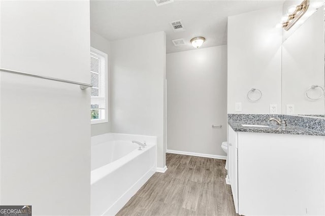 bathroom featuring vanity, a tub to relax in, toilet, and hardwood / wood-style flooring