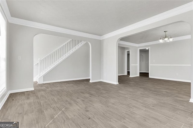 empty room featuring wood-type flooring, crown molding, and an inviting chandelier