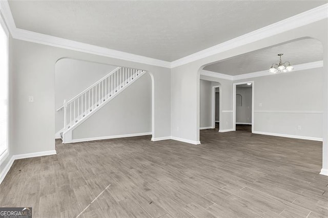 unfurnished living room with wood-type flooring, a textured ceiling, a chandelier, and ornamental molding