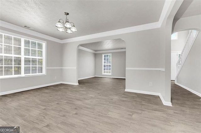 empty room featuring ornamental molding, hardwood / wood-style floors, an inviting chandelier, and a textured ceiling