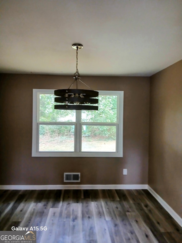 unfurnished dining area featuring a notable chandelier, dark hardwood / wood-style flooring, and a wealth of natural light