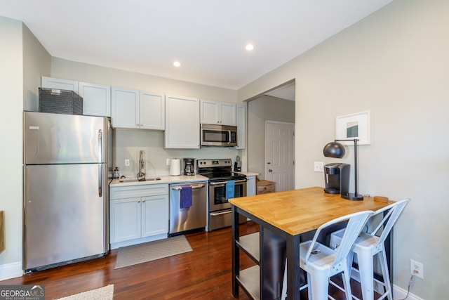 kitchen featuring dark hardwood / wood-style floors, white cabinets, sink, appliances with stainless steel finishes, and a kitchen bar