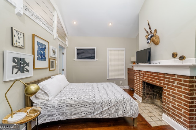 bedroom with a brick fireplace, vaulted ceiling, and wood-type flooring