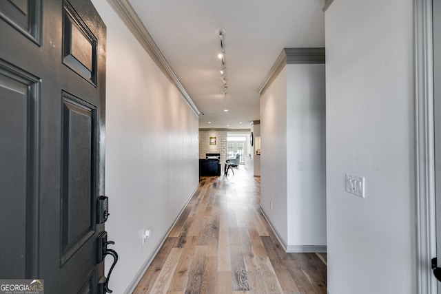 corridor with rail lighting, light hardwood / wood-style floors, crown molding, and a textured ceiling