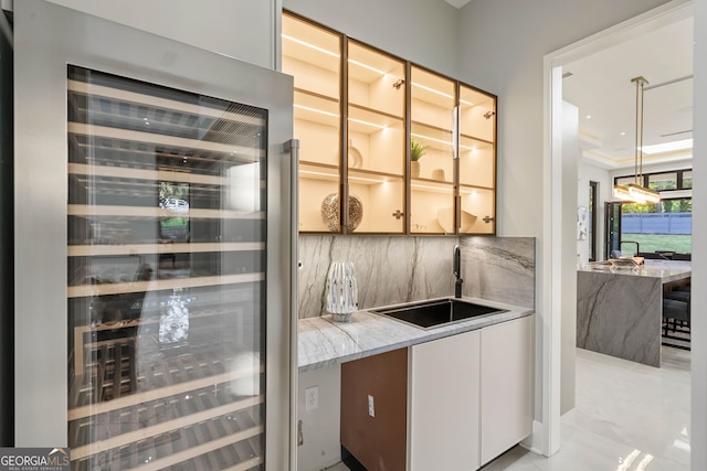 bar featuring sink, hanging light fixtures, white cabinetry, wine cooler, and decorative backsplash