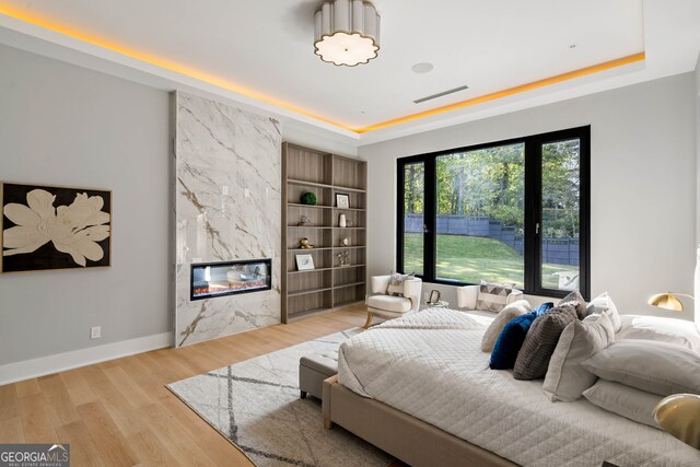 bedroom with a high end fireplace, a tray ceiling, and light wood-type flooring