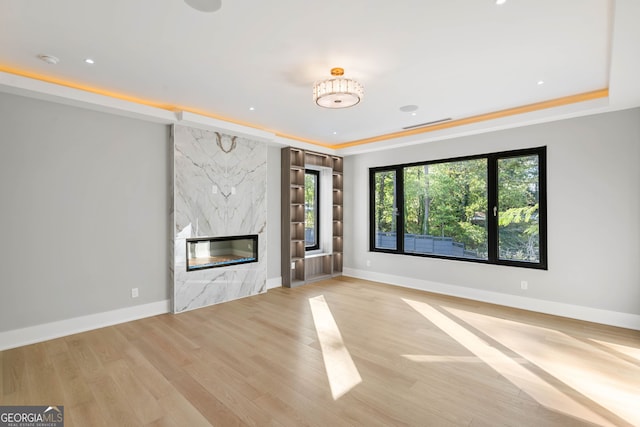 unfurnished living room with light hardwood / wood-style flooring, a high end fireplace, and a tray ceiling