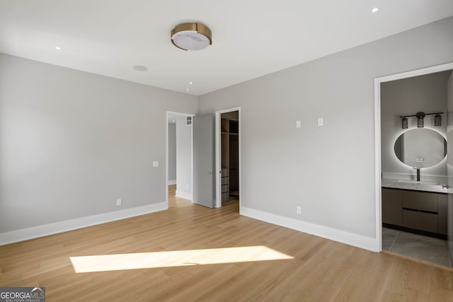 unfurnished bedroom with a closet, ensuite bath, light hardwood / wood-style flooring, and a walk in closet