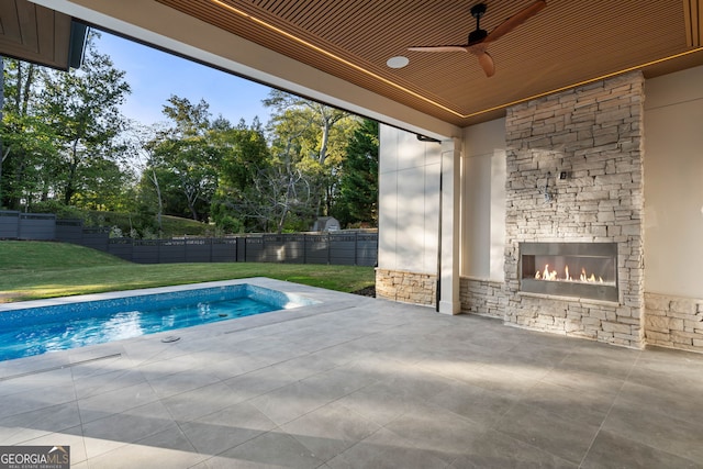 view of swimming pool with a patio, an outdoor stone fireplace, a lawn, and ceiling fan