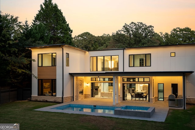 back house at dusk featuring a patio, an outdoor fire pit, a pool with hot tub, and a lawn