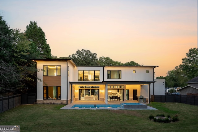 back house at dusk featuring a patio, a fenced in pool, a lawn, and a balcony